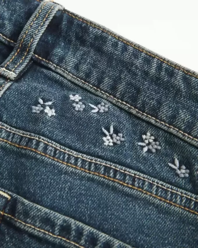 Hoch geschnittene Schlagjeans mit dunkler Waschung und Blumenstickerei Hoch geschnittene Schlagjeans mit dunkler Waschung und Blumenstickerei
